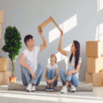 Family sitting on floor of new home, holding cardboard roof over child, symbolizing home ownership.